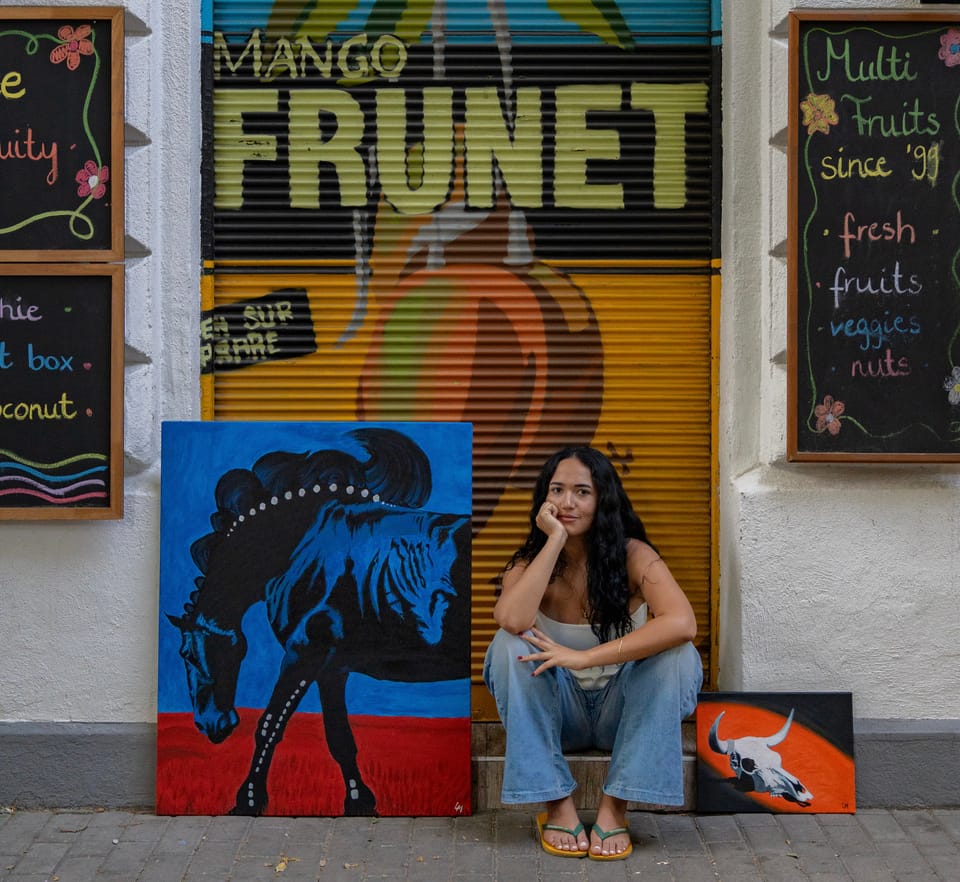 Laura Mendonzza sitting in a Budapest street between two of her paintings